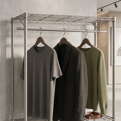 Three garments hanging on a metal clothing rack in an indoor room: a heather gray short-sleeve T-shirt, a dark charcoal blazer, and an olive green knit sweater. The rack is positioned against a textured concrete wall.