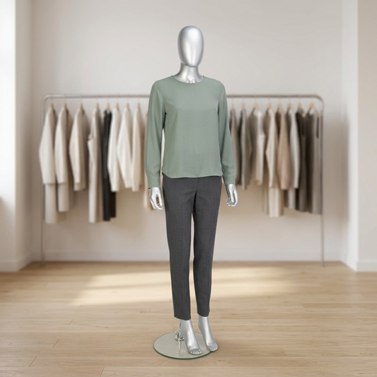 Female gloss-silver Candor faceless mannequin displaying sage blouse and charcoal trousers in a neutral boutique